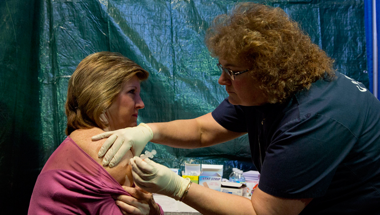 Man wearing latex gloves giving woman a vaccine injection.