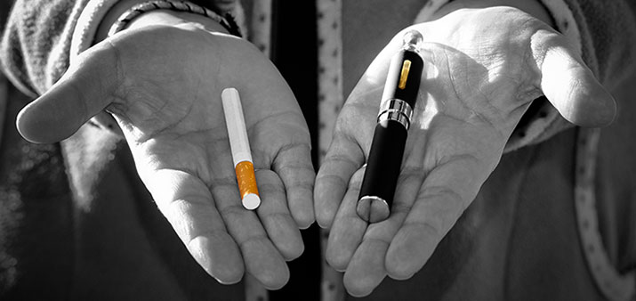 Hands holding a tobacco cigarette and an e-cigarette.