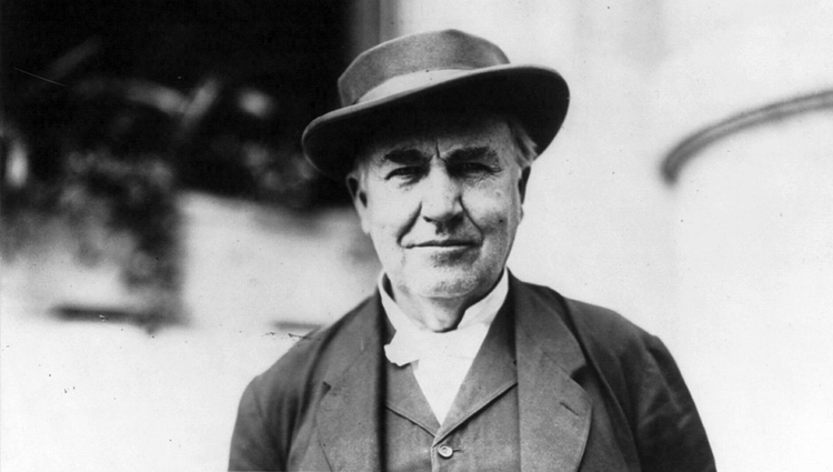 Thomas A. Edison in hat and coat, outdoors. 