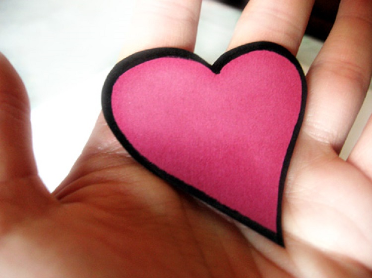 A plam-sized pink cushion heart with black trim held in a hand. 