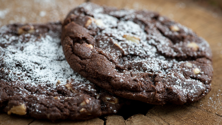 Two chocolate cookies coated in powdered sugar. 