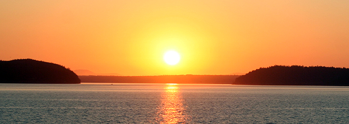 The sun, low over the water in a hazy sky. 