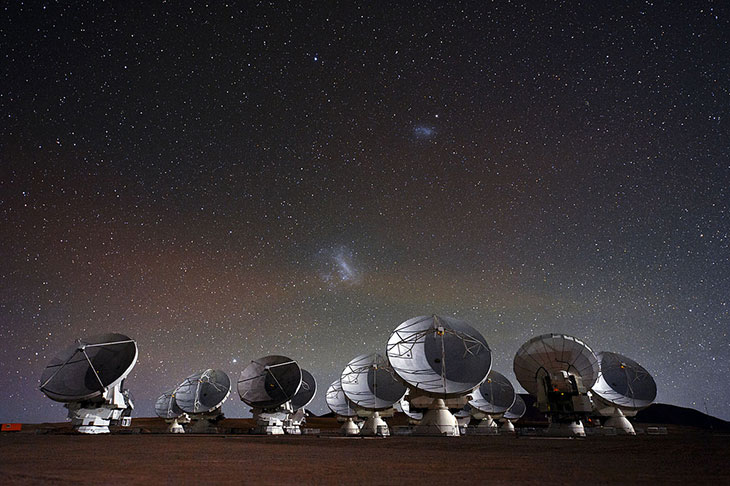 The Large and Small Magellanic Clouds are visible in the sky above the Atacama Large Millimeter/submillimeter Array (ALMA), a radio telescope in Chile.