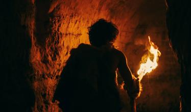 A cave man carries a torch into a cave.