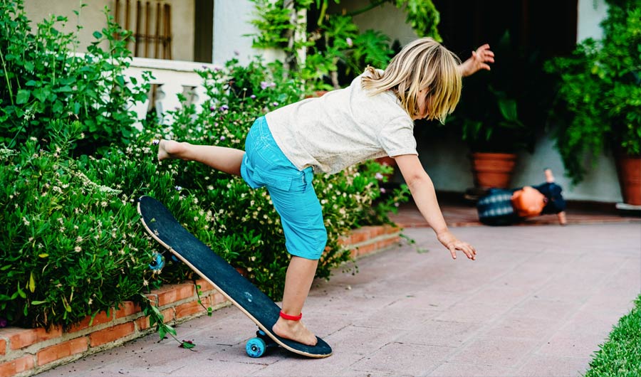 Blonde boy falling off skateboard, rear view. 
