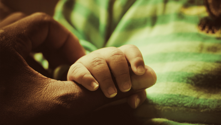 Father's hand gently enclosed around baby's wrist. 