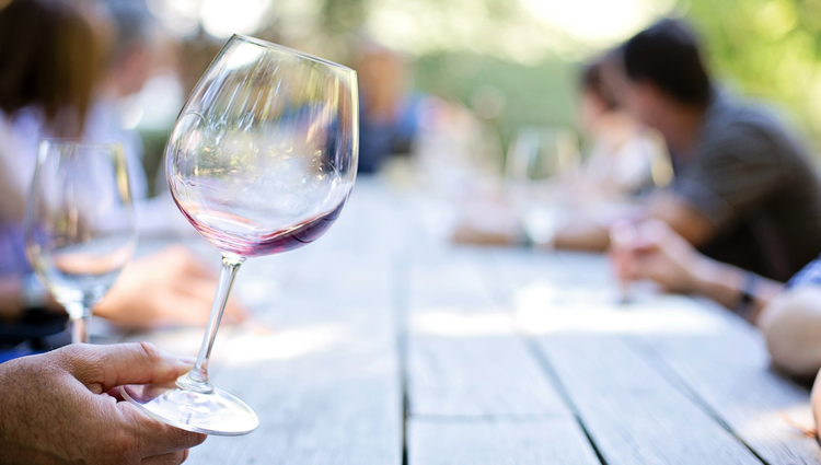 People eating over a picnic table, focus on nearly empty red wine glass. 