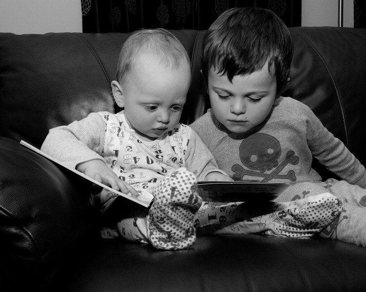 Toddler and infant sharing a book. 