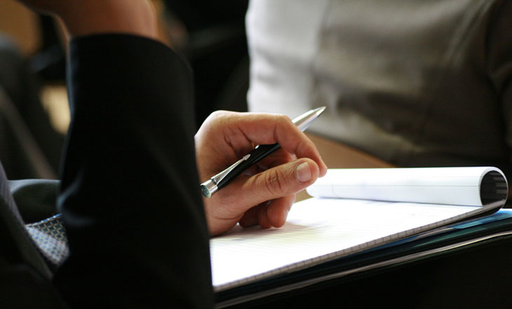 Left-hand holding pen over a paper tablet.