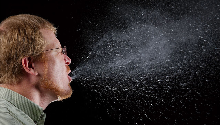 Side view of man sneezing, highlighting droplets projecting far from head. 
