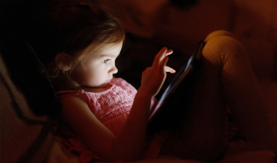 Child reading illuminated screen in the dark. 