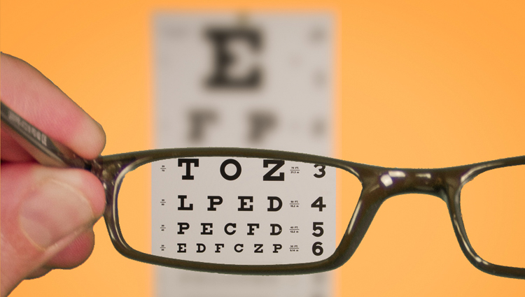 Glasses held in front of an eye exam chart. 