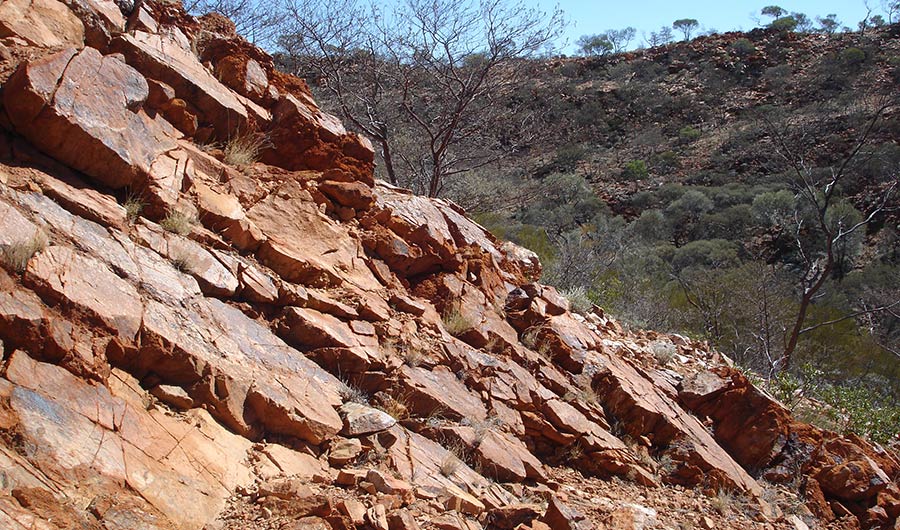 Landscape with jagged, red-tinged rocks, in a dry climate with brush in the background.